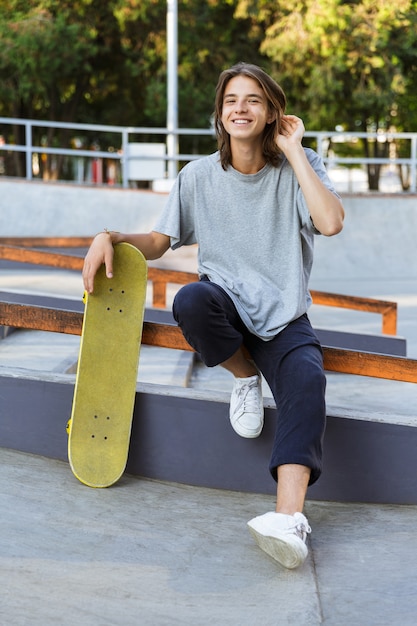 Image of handsome young skater guy sit in the park with skateboard.