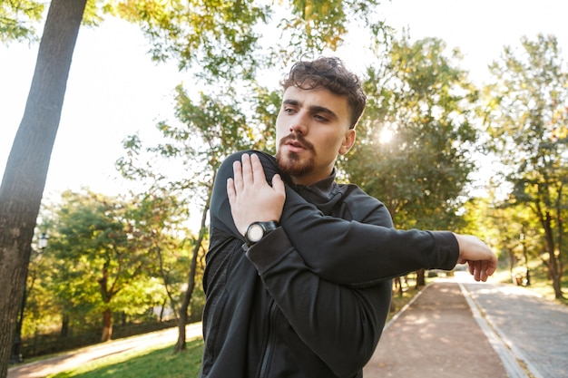 Image of handsome young sports fitness man runner outdoors in park make exercises.