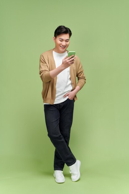 Image of happy asian man holding cellphone while standing isolated by light green background