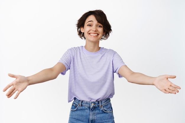 Image of happy beautiful girl extend her hands, reaching for hug, cuddles, warm friendly welcome, greeting you, smiling cheerful, standing over white background.