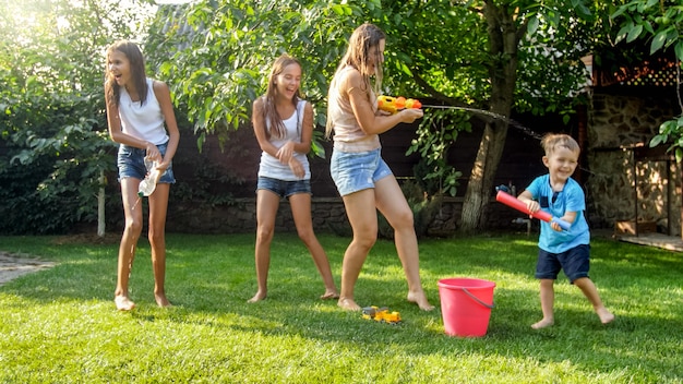 Image of happy cheerful children wuth young mother playing with water guns and garden house. Family playing and having fun outdoors at summer