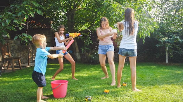 Image of happy cheerful family playing in the backyard garden. People splashing water with water guns and garden hose.