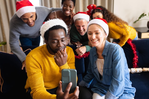 Photo image of happy diverse friends celebrating christmas at home making smartphone video call. christmas, celebration, tradition, friendship, inclusivity and lifestyle concept.