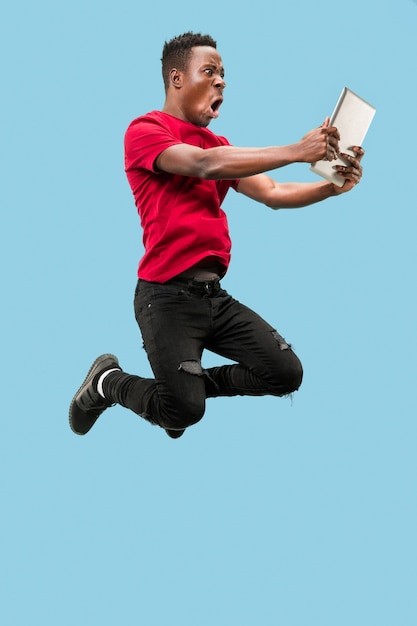 Photo image of happy excited young african man jumping isolated over yellow background using laptop