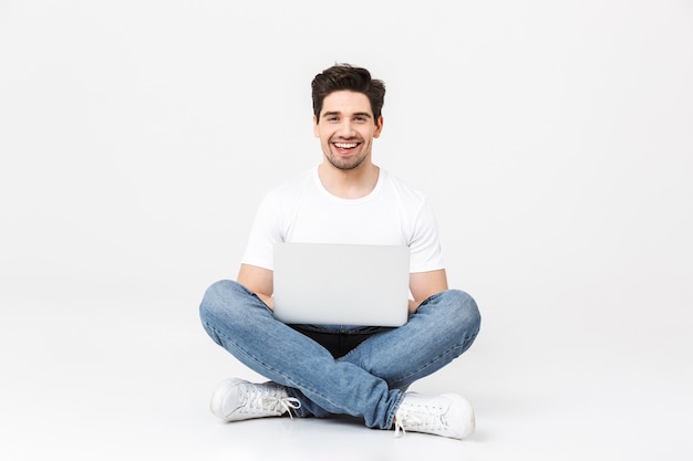 Image of happy excited young man posing isolated over white wall using laptop computer.