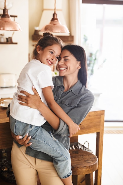 Foto immagine di una madre di famiglia felice che sorride e tiene in mano la sua piccola figlia mentre riposa in un accogliente appartamento