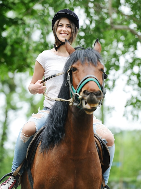 Immagine della femmina felice che si siede sul cavallo all'azienda agricola del villaggio