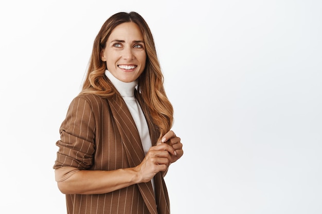 Изображение счастливой женщины средних лет в элегантном костюме, смотрящей в сторону на рекламный баннер продукта, улыбающейся и смеющейся на белом фоне