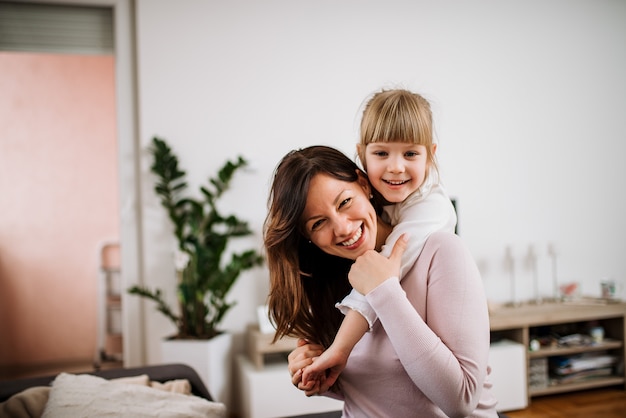 Image of a happy mother piggybacking adorable little daughter. Looking at camera