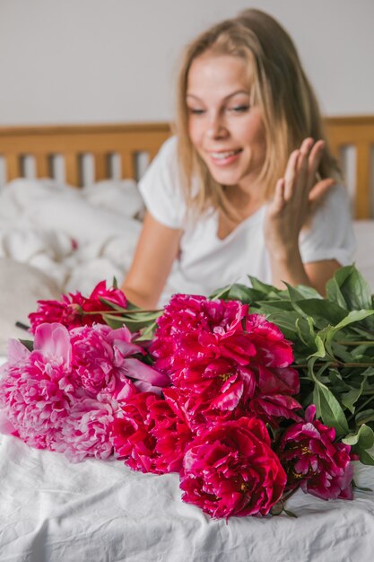 L'immagine di una giovane donna felice e positiva al chiuso a casa in camera da letto a letto con in mano dei fiori si fa un selfie con il cellulare.