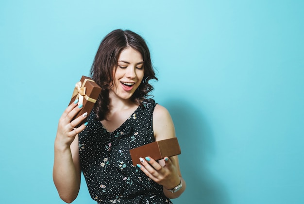 The image of a happy smiling woman opening a gift box and showing isolated gestures over blue wall