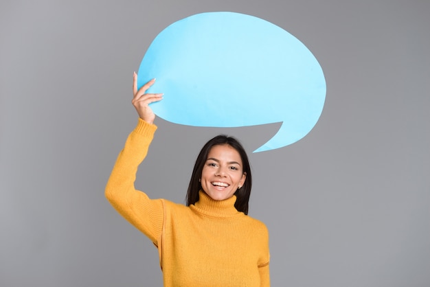 Image of a happy woman posing isolated over grey wall holding speech bubble.