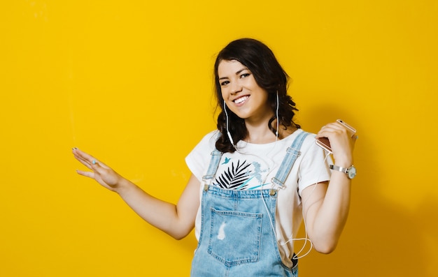 Image of happy woman wearing earphones singing isolated over yellow wall