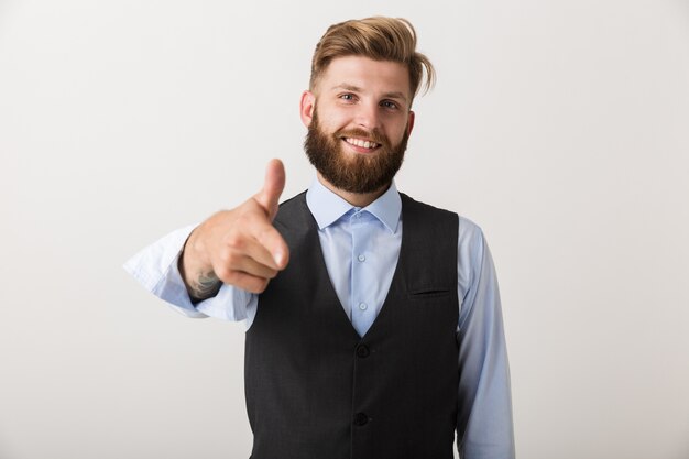 Image of a happy young bearded man standing isolated over white wall pointing.