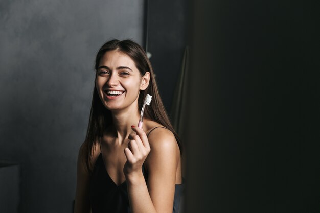 Image of a happy young beautiful woman in bathroom brushing her teeth.