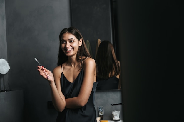 Image of a happy young beautiful woman in bathroom brushing her teeth.