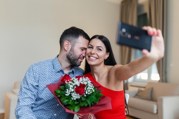 Image of happy young couple taking selfie photo with flowers while having a romantic time at home Lovely couple celebrating Valentine's Day