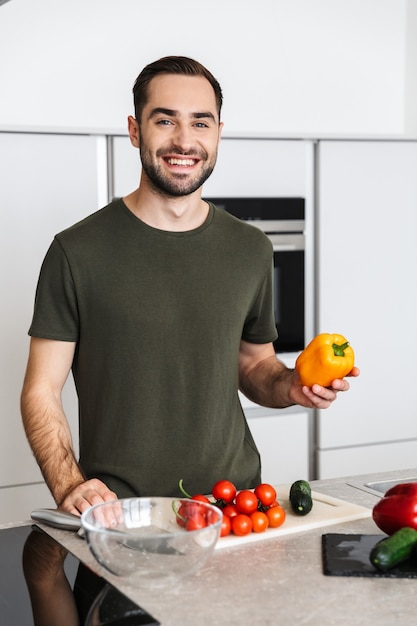 自宅のキッチンで料理をしている幸せな若いハンサムな男の画像は、朝食を持っています。