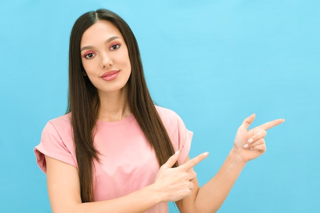 Image of happy young lady standing isolated on blue background Looking at camera pointing finger