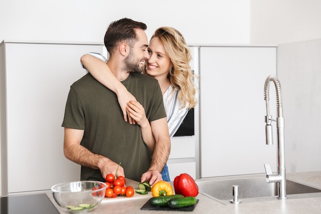 Изображение счастливой молодой любящей пары, позирующей на кухне дома для приготовления завтрака, обниматься.