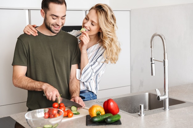 Image of a happy young loving couple posing at the kitchen at home cooking have a breakfast hugging.