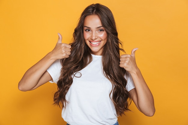 Image of happy young woman isolated over yellow wall showing thumbs up gesture.