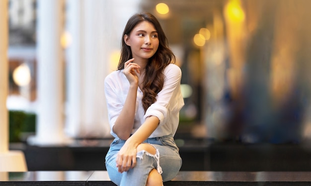 Image of happy young woman sitting on the floor at night on city