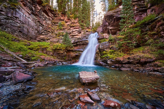 Изображение скрытого секретного водопада, струящегося из каньона в каменный каньон с одинокой скалой