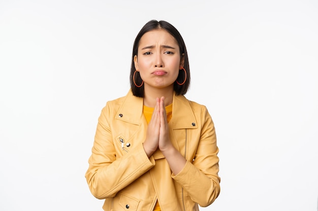 Image of hopeless asian woman begging pleading say sorry looking distressed and miserable standing over white background