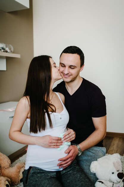 Image of husband holding belly of his pregnant wife socks for baby in hands Pregnant woman or girl and loving handsome man hugging tummy at home Loving Couple Parenthood concept Baby Shower