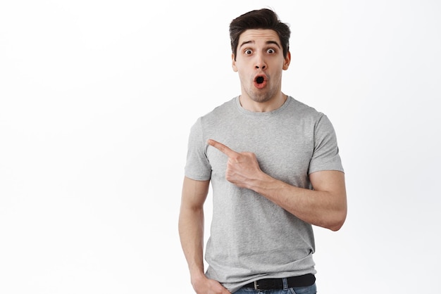 Image of impressed handsome man drop jaw gasping and look amazed pointing left at promo copyspace white background