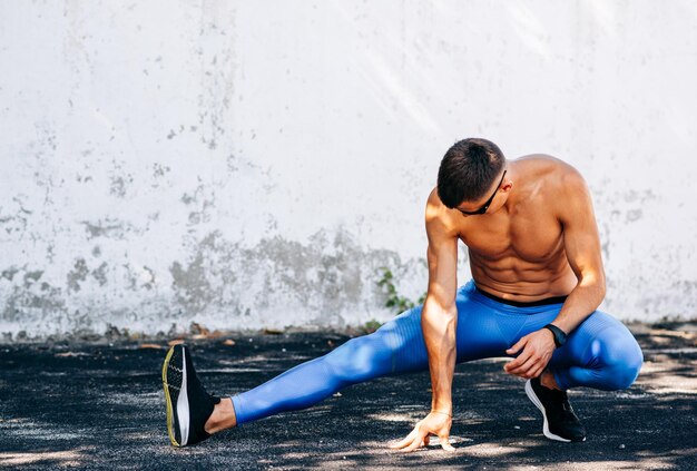 Image of jogger man stretching before exercises outdoors against concrete wall Athlete male stretches after workout outside Sport and people concept Copy space for your text