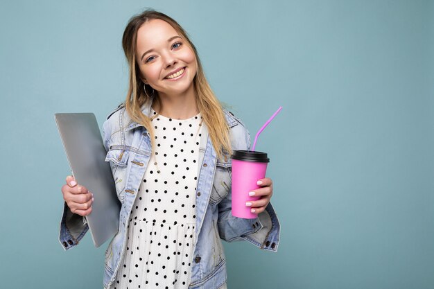 Image of joyful european blond woman smiling and standing against blue wall isolated with silver