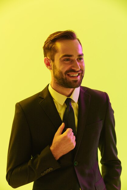 Изображение радостного молодого бизнесмена в строгом костюме, улыбающегося в камеру, изолированную над желтой стеной