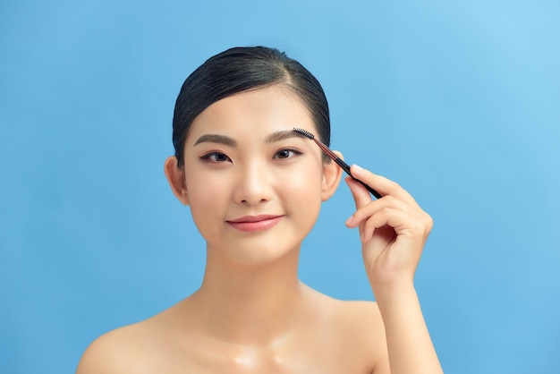 Image of joyful young shirtless woman using eyebrows brush and smiling isolated over grey background