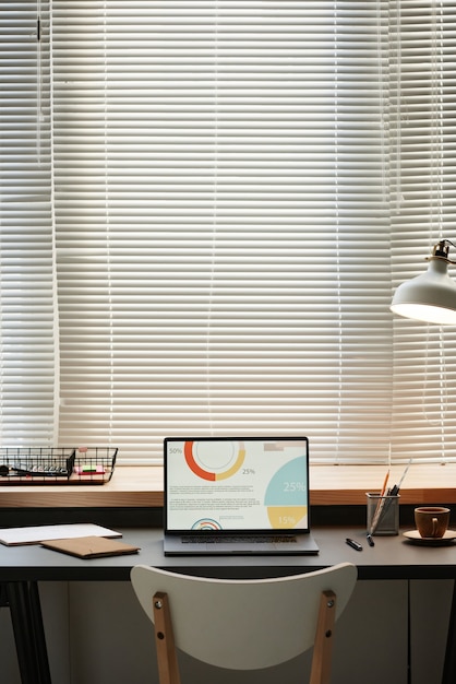 Image of laptop with financial charts on the screen on the\
table in front of the big window at office