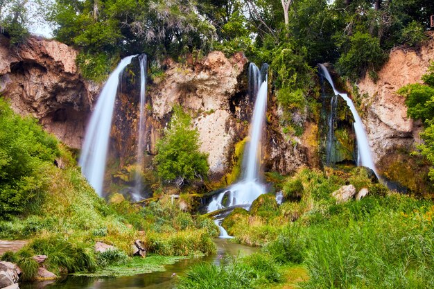 Image of Large triple waterfalls over cliffs in lush green forest landscape