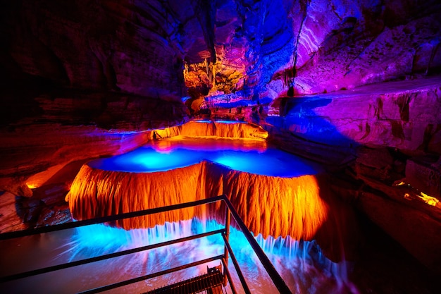 Image of Large underground waterfall in cave on tour path with orange and blue lights