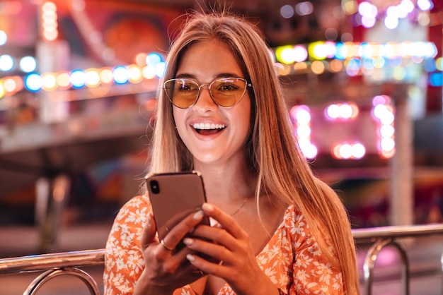 Image of laughing happy woman walking outdoors in amusement park using mobile phone.