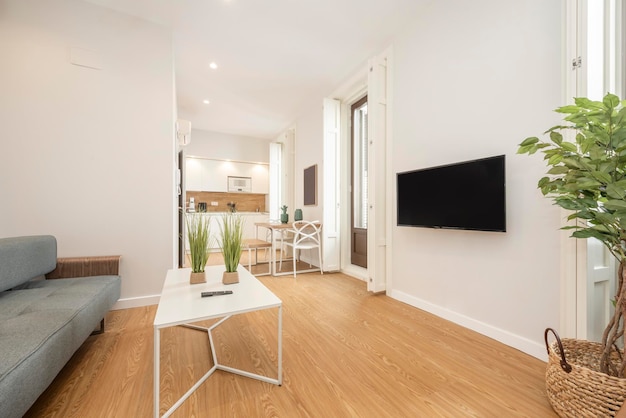 Image of a living room with large windows tv and an office table and kitchenette in the background in a vacation rental studio