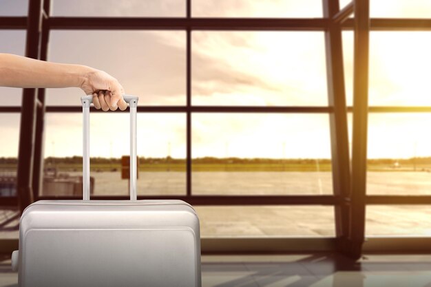 Image of man hand holding soft grey suitcase with airport view on background