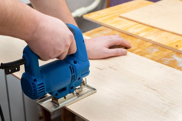 Image of a man hand using electric jigsaw. close up process of cutting wooden board.