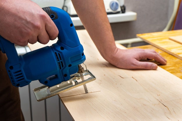 Image of a man hand using electric jigsaw. close up process of cutting wooden board.