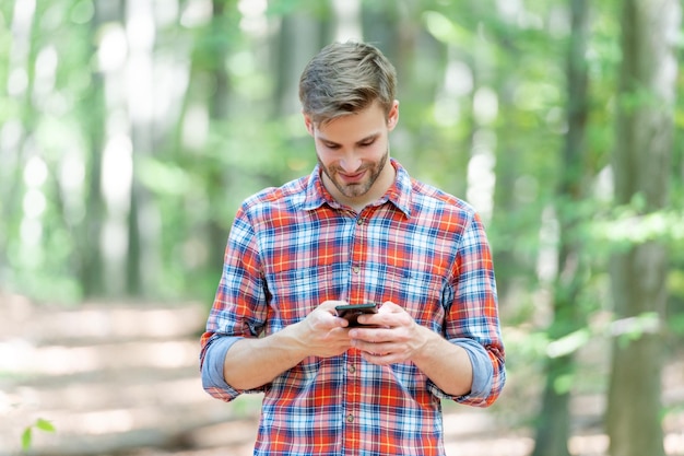 Image of man messaging on phone in the forest man messaging on phone outdoor man messaging on phone outside man messaging on phone wearing checkered shirt