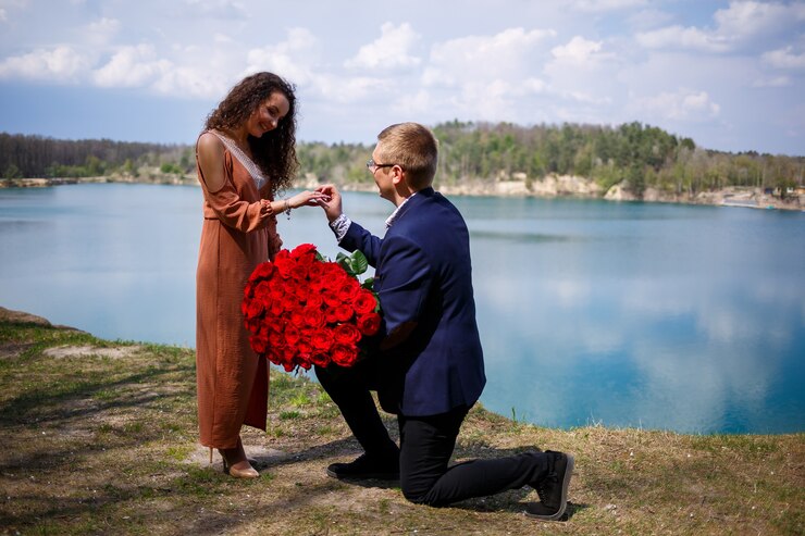Photo image of a man putting a silver wedding ring on a woman's hand, outdoors. sea or river background
