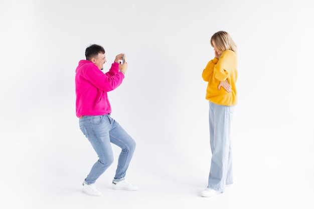 Image of a man take photo of his positive optimistic woman on white background by mobile phone