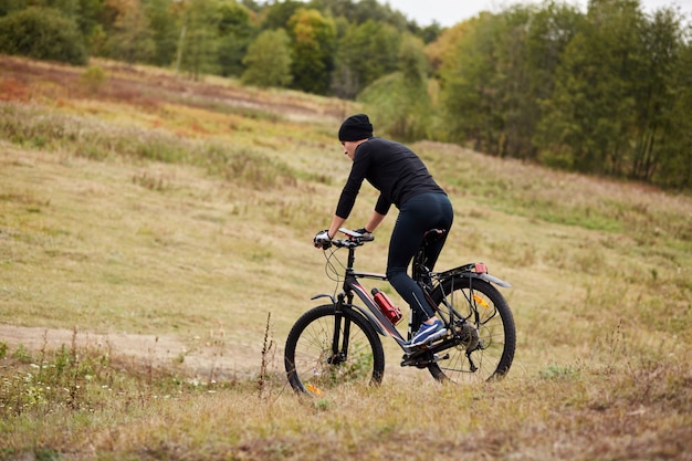 Immagine del ciclista della bici della montagna in prato vicino alla foresta, vista laterale della bici di guida maschio sportiva durante la sua vacanza