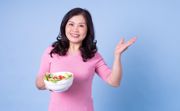 파란색 배경에 샐러드를 먹는 중년 아시아 여성의 이미지