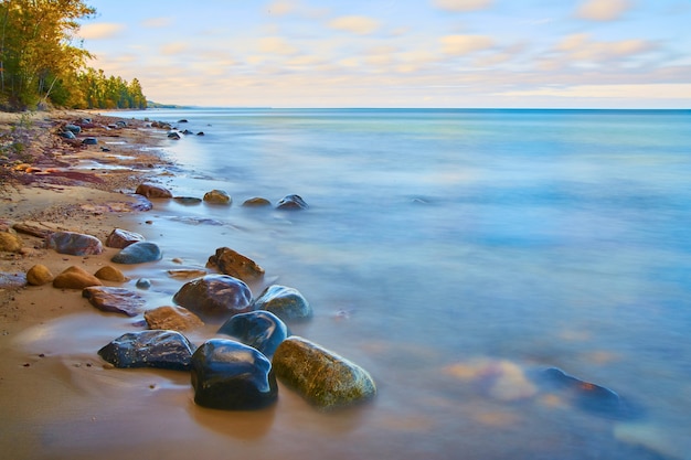 Image of Misty lake surface with wet smooth rocks against a sandy shore with a forest