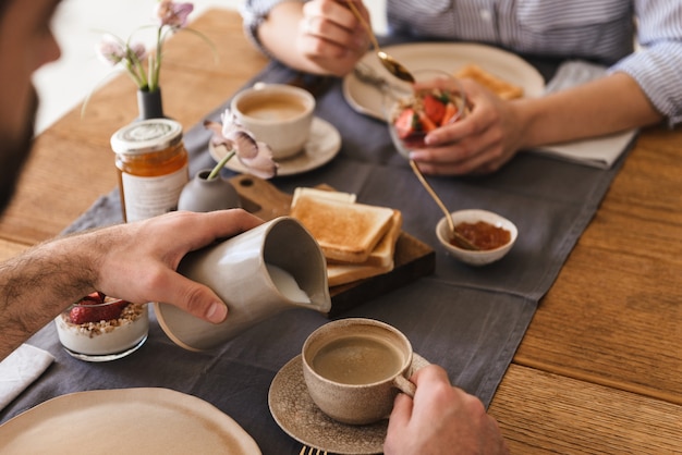 Immagine di una moderna coppia felice uomo e donna che mangiano insieme a tavola mentre fanno colazione in appartamento
